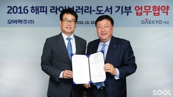 지난 18일 서울 강남 오비맥주 본사에서 오비맥주 정책홍보담당 장유택 전무(왼쪽)와 대교 사회공헌실 서명원 실장이 ‘2016 해피 라이브러리-도서 기부’ 업무협약(MOU)을 체결한 후 기념촬영을 하고 있다.