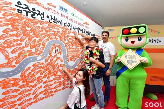 오비맥주가 21일 도로교통공단과 함께 서울 강남운전면허시험장에서 신규 운전면허 취득자를 대상으로 음주운전 예방 캠페인을 펼쳤다. &lsquo;음주운전 안하기 다짐 서약&rsquo;에 참여한 새내기 운전자들이서약 스티커에 직접 서명을 한 뒤오비맥주 김도훈 대표와 함께 안전운행 도로 서약판에부착하고 있다.