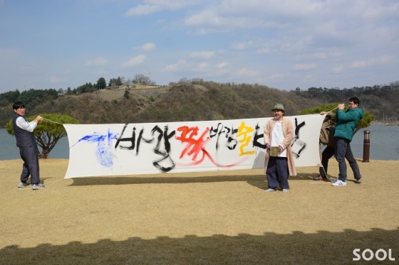 김기상 화백이 ‘강바람 꽃바람 술 바람’이란 휘호를 퍼포먼스로 쓰고 있다.